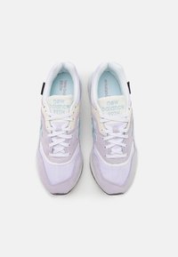 Un paio di sneakers New Balance 997H in lavanda e bianco con dettagli azzurri chiari e lacci bianchi, viste dall'alto su uno sfondo bianco.