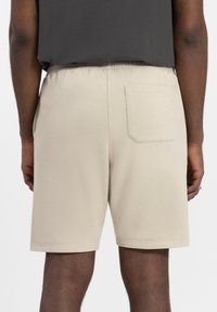Lichtbeige shorts met een elastische tailleband, één achterzak en een gladde katoenachtige textuur. Eenvoudig ontwerp zonder patronen of accenten.