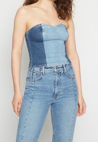 Jeanslinne utan axelband med ljusblå och mörkblå paneler, figurnära passform, slät textur och hjärtformad halsringning. Kombinerat med högmidjade jeans.