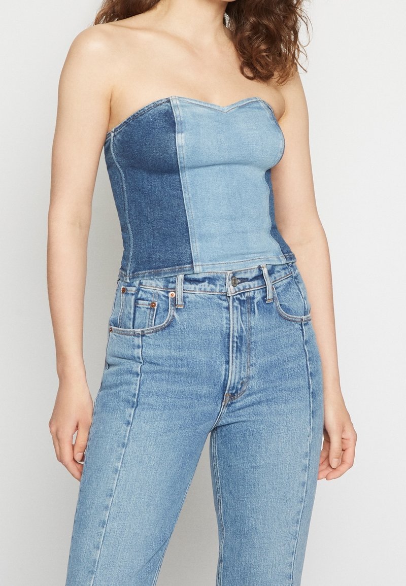 Jeanslinne utan axelband med ljusblå och mörkblå paneler, figurnära passform, slät textur och hjärtformad halsringning. Kombinerat med högmidjade jeans.