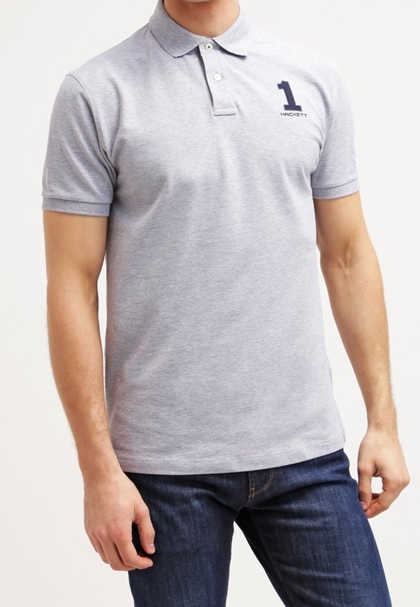 Muž oblečený v svetle šedém polo tričku s logem "1 Hackett" na levé straně hrudi, doplněný tmavě modrými džínami.