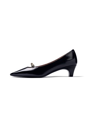 Zapato negro de charol con tacón bajo, puntera puntiaguda y pequeña decoración metálica en forma de lazo en la parte superior, vista lateral sobre fondo blanco.