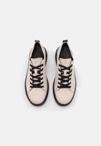 Helle beige Leder-Sneaker mit schwarzen Schnürsenkeln, runder Zehenpartie und einer schwarzen Gummisohle. Verfügt über eine Schlaufe an der Rückseite für einfaches An- und Ausziehen.