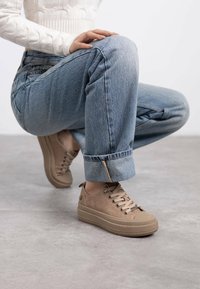 Zapatillas de plataforma beige con textura de ante, puntera redonda y diseño de cordones. Combinadas con unos jeans de mezclilla desgastados y con dobladillo.