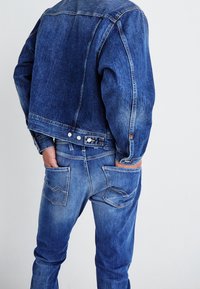 Džinová bunda s mírně zkráceným střihem, džíny s gradientem od světle modré po tmavě modrou, viditelné švy a dvě zadní kapsy s zakřivenými vzory.