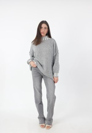 Grijze gebreide trui met een hoge kraag en zilverkleurige accenten op de mouwen, gedragen met lichtgrijze flare broek. Glad oppervlak, ontspannen pasvorm.