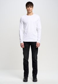 Hvid langærmet T-shirt lavet af bomuld, parret med sorte jeans og sorte sneakers. Simpelt design med rund halsudskæring og tætsiddende silhuet.