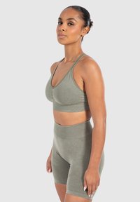 Conjunto de ropa deportiva verde con una tela texturada y elástica. El sujetador tiene un escote en V y tirantes finos; los pantalones cortos de tiro alto presentan acentos acanalados.