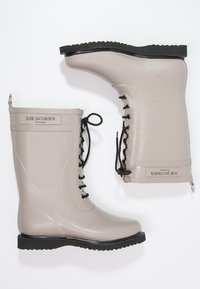 Bottes de pluie en caoutchouc gris clair avec une semelle noire texturée, lacets à l'avant et une languette; comporte le logo de la marque sur le côté.