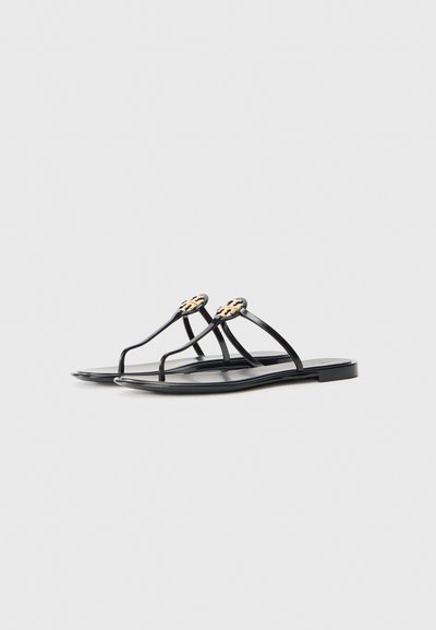 Sorte flate sandaler med tynne stropper og en distinkt logo i gull. Glatt, matt fotseng med et minimalistisk design.