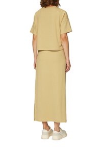 Beige twee-delige outfit met een gestructureerde losse top met korte mouwen en een bijpassende lange rok met zijsplitten, gecombineerd met platte sneakers.