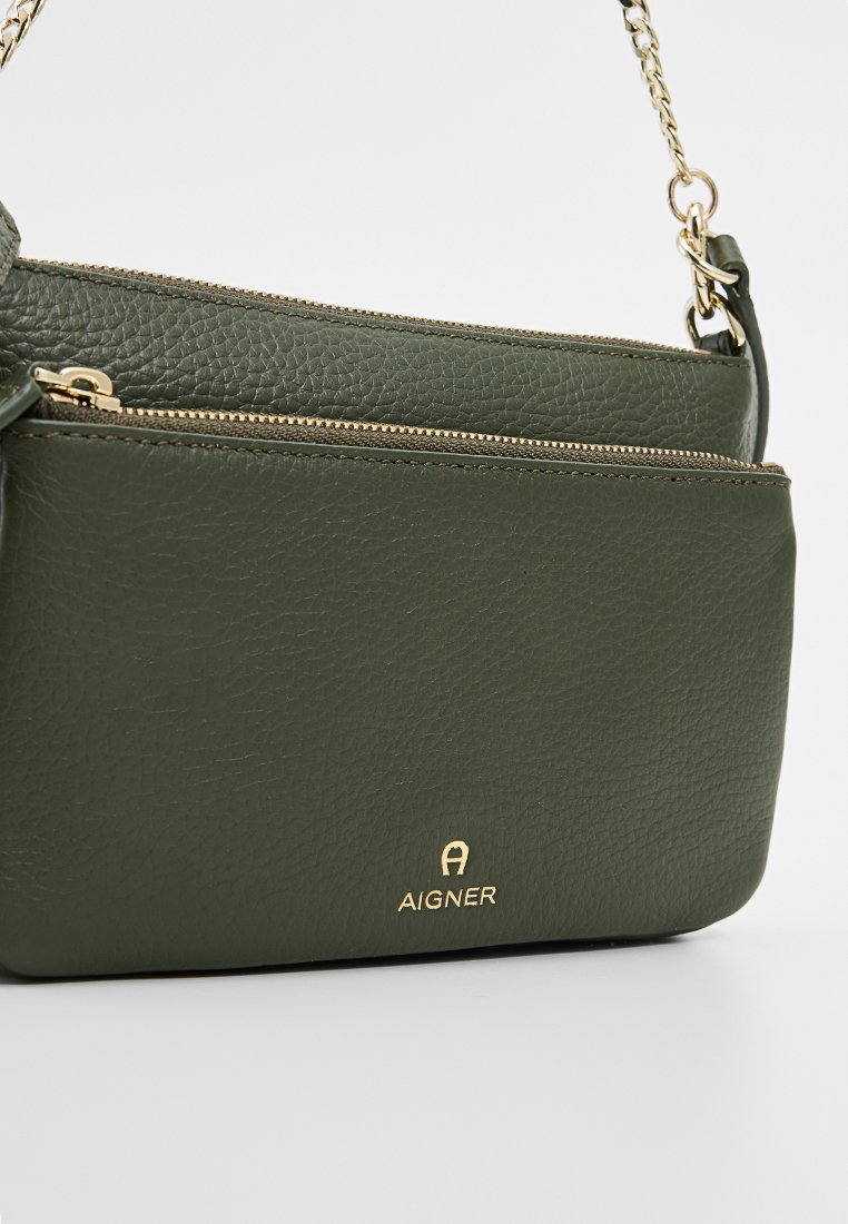 Grüne Lederhandtasche mit strukturiertem Oberflächen, zwei Reißverschlussfächern und einem goldenen Logo auf der Vorderseite. Ausgestattet mit einem Schultergurt aus Metallkette.