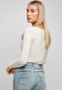 Blusa de manga larga crema combinada con jeans de cintura alta en azul claro, con un diseño ajustado y bolsillos traseros. Textura suave con acentos mínimos.