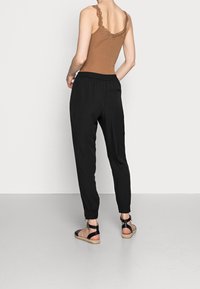 Top corto marrón con encaje, pantalones jogger negros con cintura elástica y sandalias negras con correas en el tobillo y suelas trenzadas.