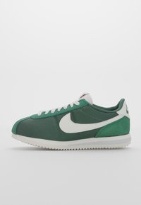 Green Nike sneakers with a canvas upper, white swoosh, textured detailing, and a rubber sole featuring small lugs for traction.