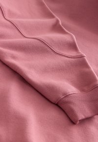 Manche de sweat-shirt rose doux avec poignet côtelé et détail de couture visible sur tissu lisse.