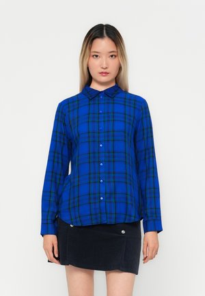 Blue and green plaid button-up shirt with long sleeves and a collared neckline, paired with a black skirt featuring decorative buttons.