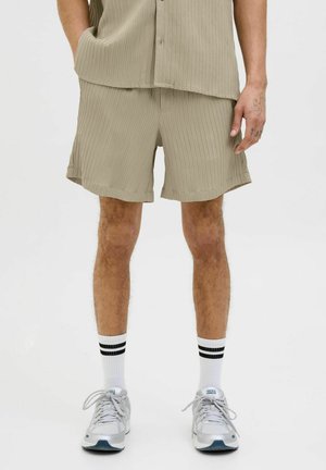 Light beige ribbed shorts made of textured fabric, featuring a relaxed fit, and paired with white socks and gray sneakers.