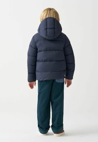 Giacca puffer blu navy con cappuccio, con sezioni cucite per l'isolamento. Abbinata a pantaloni in corduroy verdi a vestibilità ampia e scarpe bianche.