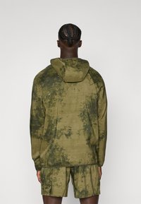 Veste à capuche vert olive avec un motif camouflage texturé ; associée à un short assorti. Le design présente des manches longues et une coupe décontractée.