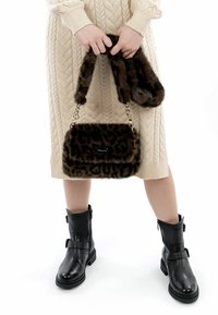Borsa in pelliccia sintetica con stampa leopardata marrone e catena dorata, portata con un manico abbinato. Abbinata a un vestito a maglia color crema e stivaletti neri.