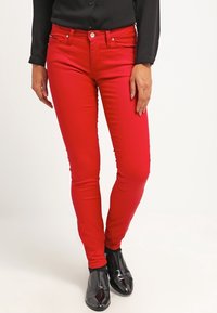 Czerwone dżinsy slim fit wykonane z rozciągliwej bawełny, z pięcioma kieszeniami i zamek błyskawiczny. W zestawie z czarną bluzką i błyszczącymi czarnymi botkami na kostkę.