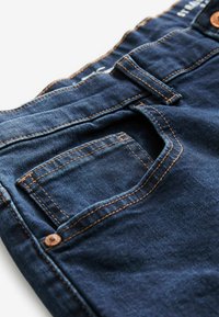 Donkerblauwe spijkerbroek van denim met een gestructureerde afwerking, voorzien van oranje stiksels, een voorzak en een riemlus op de tailleband.