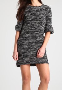 Robe texturée en noir et blanc avec des manches courtes bouffantes. Présente un col rond et une silhouette ajustée, longueur genou avec un motif subtil.