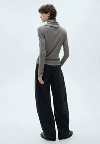 Siv turtleneck pulover z rebrastim vzorom, sproščenega kroja, v kombinaciji z visokimi črnimi širokimi hlačami, obutimi z ravnimi črnimi čevlji.