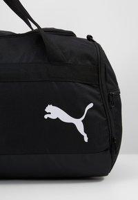 Borsa da viaggio nera in tessuto resistente, con chiusura a zip, tracolla regolabile e logo bianco Puma ben visibile sul lato.