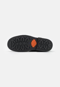 Suela de zapato de goma negra con un patrón de agarre texturizado, con un logo de Harley-Davidson en color naranja destacado en la zona del talón.