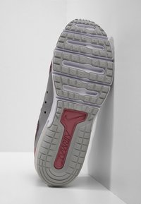 Semelle extérieure de chaussure de sport grise avec une surface en caoutchouc texturée, des crampons proéminents et un accent rouge Nike Air Max près du talon.