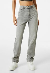 Vaqueros grises de talle alto con un ajuste holgado, combinados con un top negro corto. Las características incluyen cinco bolsillos, costuras en contraste y un cierre de botón.