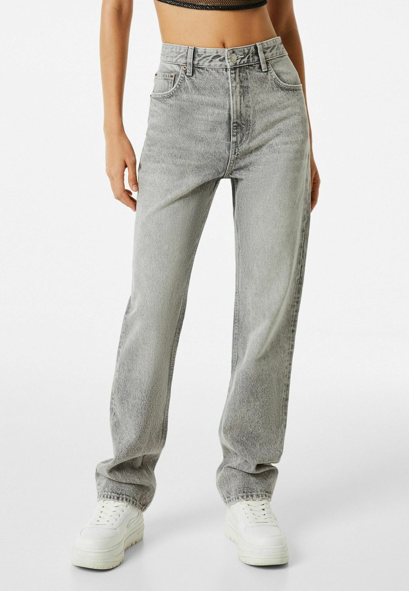 Vaqueros grises de talle alto con un ajuste holgado, combinados con un top negro corto. Las características incluyen cinco bolsillos, costuras en contraste y un cierre de botón.