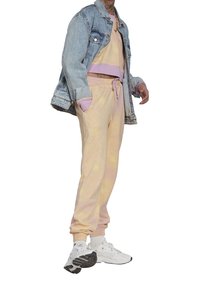 Džínová bunda přes pastelový tie-dye svetr a tepláky s elastickými manžetami a stahovacími šňůrkami v pase. Kombinováno s bílými teniskami.
