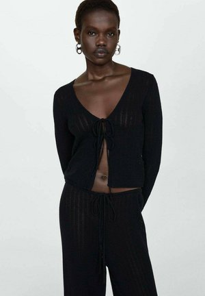 Schwarze, kurze Strickjacke mit V-Ausschnitt und gebundenem Front, kombiniert mit passenden Jogginghosen mit Kordelzug und strukturiertem Muster.