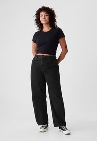 Mustat lyhyet t-paita, mustat korkeavyötäröiset farkut, rento istuvuus, kontrastivalkoiset lenkkarit. Malli seisoo neutraalisti.