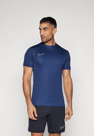 Donkerblauw sportshirt met korte mouwen, ronde hals en wit Nike-logo. Materiaal lijkt glad en aansluitend, gecombineerd met donkere shorts.
