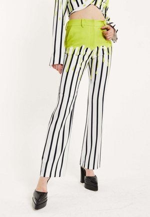 White and black striped pants with a lime green waistband and drip pattern. Flared bottom and high-heeled black shoes complete the look.