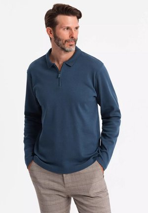 Polo de manga larga para hombre en azul oscuro, con collar con cremallera, tejido suave y textura lisa, combinado con pantalones de cuadros claros.
