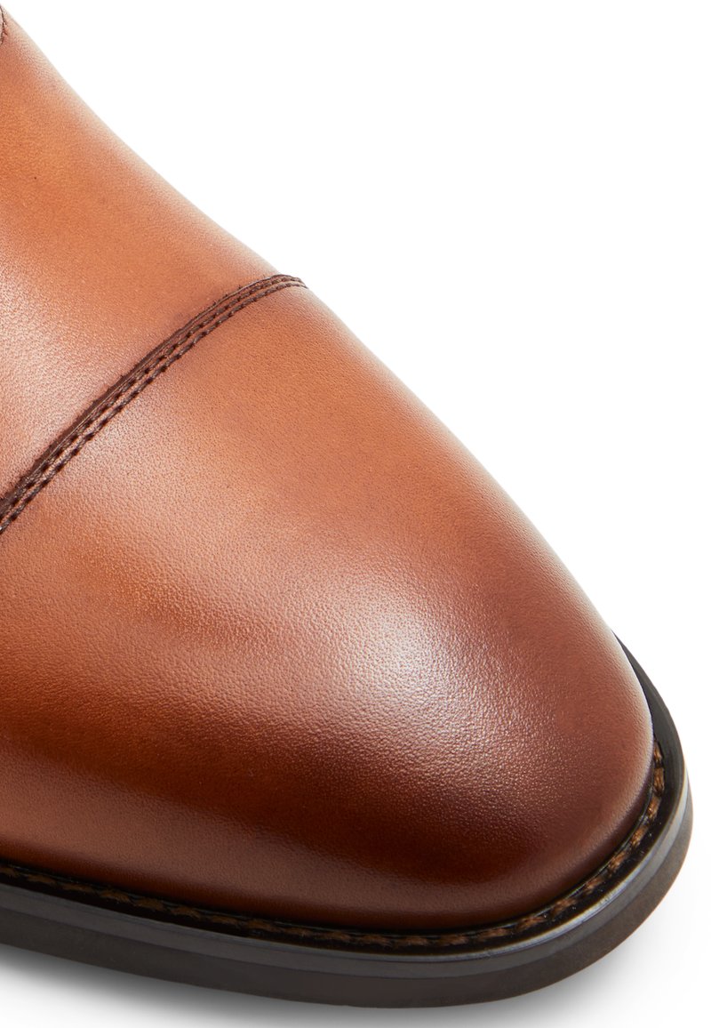 Chaussure en cuir marron avec une finition lisse, un bout arrondi et des coutures contrastantes le long du bord de la semelle. Semelle extérieure en caoutchouc noir.