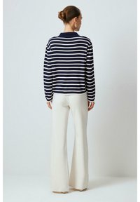 Mörkblå och vit randig stickad tröja med krage, i kombination med vita utsvängda byxor; slät textur, avslappnad passform och enkel design.