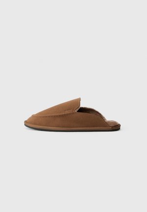 Brown suede slipper with a soft interior lining, open back design, and stitched detailing along the edges. Flat rubber outsole.