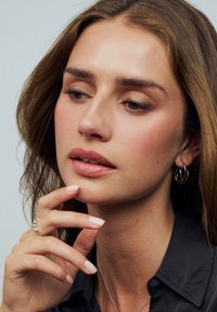 Silver hoopörhängen, slät hy, naken läppstift, långt mörkt hår, svart skjorta och en delikat silverring med små utsmyckningar.