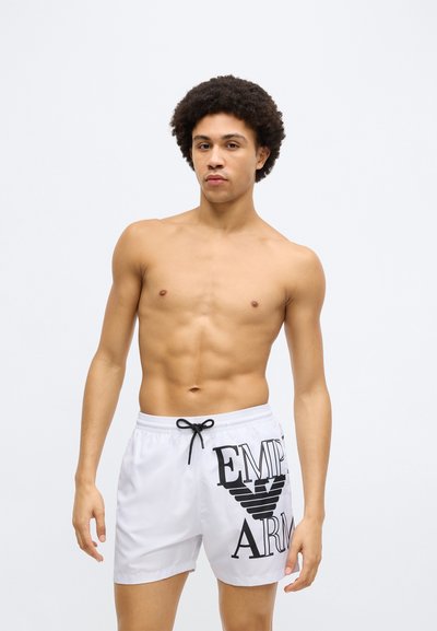 Λευκά μαγιό σορτς με μαύρο γραφικό λογότυπο "EMPIRE" και σχέδιο φτερών, με ελαστική μέση και κορδόνι.