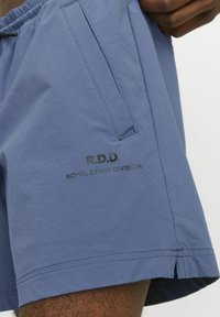 Pantalones cortos azules de tejido ligero, con un bolsillo lateral y el logo en relieve "R.D.D. ROYAL DENIM DIVISION" en la pierna.