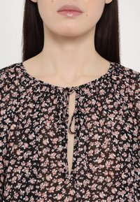 Musta kukkakuosisalamat, joissa on avonainen kaula-aukko, vaaleanpunaisia ja valkoisia kuvioita, koottua kangasta sekä nyörikiinnitys kaulalla.