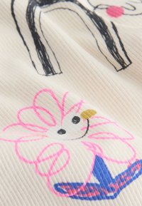 Tessuto bianco con texture a coste che presenta un disegno a linee nere di un cane e un motivo floreale rosa e blu con un centro nero e giallo.