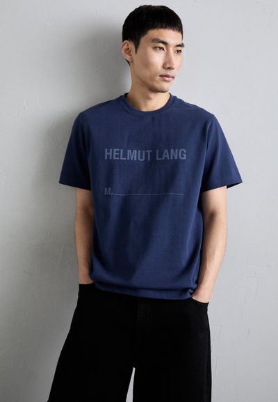 Marineblå bomull T-skjorte med trykk foran med "HELMUT LANG" og en tom linje. Korte ermer, rund hals og avslappet passform.