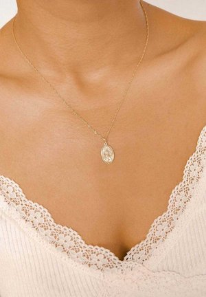 Goldene Kettenhalskette mit einem detaillierten ovalen Anhänger mit floralem Design, getragen über einem cremefarbenen Oberteil mit Spitzenbesatz.